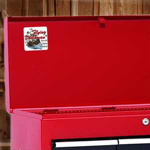 Red metal tool chest with a Flying Dutchman Scroll Saw Blade sticker in front of a wood slat wall.